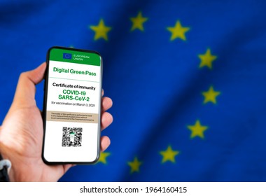 The digital green pass of the european union with the QR code on the screen of a mobile held by a hand with a blurred EU flag in the background. Immunity from Covid