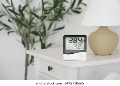 Digital hygrometer and lamp on table in bedroom, closeup