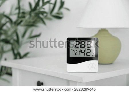 Digital hygrometer and lamp on table in bedroom, closeup