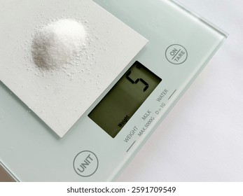A digital kitchen scale displays a precise measurement of 5 grams of salt on a small card, illustrating the recommended daily sodium intake for health-conscious nutrition