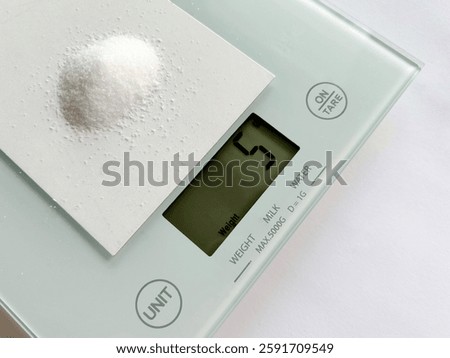 A digital kitchen scale displays a precise measurement of 5 grams of salt on a small card, illustrating the recommended daily sodium intake for health-conscious nutrition