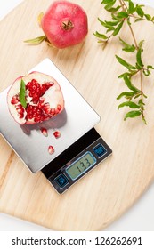 Digital kitchen scale on table and pomegranate.