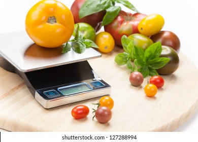 Digital kitchen scale on table surrounded with fresh tomatoes, and basil.