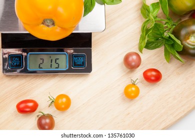 Digital kitchen scale on table surrounded with fresh tomatoes, and basil.