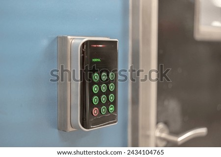 A digital locking keypad device which is installed on the blue wall infront of the entry door. Technology equipment object photo, selective focus.