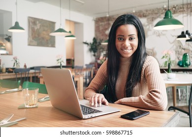 Digital marketing specialist is working on a new promotion project by a portable computer while sitting in a modern coffee shop during lunch time. Freelancer female is communicating with customers.