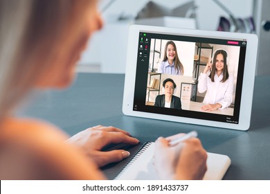 Digital Meeting. Corporate Videocall. Web Chat. Distance Work. Pandemic WFH. Diverse Multiracial Team In Headphones Discussing Project On Tablet Screen Female Employee Taking Notes At Home Office.