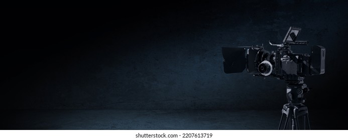 Digital movie camera in the dark. Video camera on a tripod in a black contre room with light and shadow. Tv documentary or movie production banner background with copy space