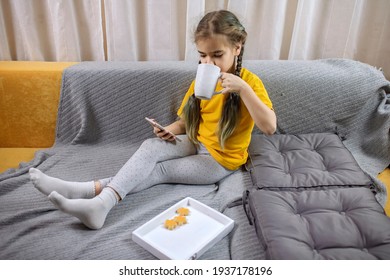 Digital native generation alpha, cute kid lying on yellow sofa with gray blanket and using smartphone for chatting and distant learning, online education at home, new normal lifestyle, trendy colors