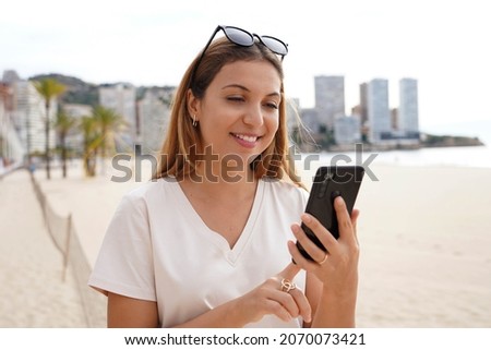 Digital nomad. Attractive millennial freelancer working reading messages during virtual chatting remotely near the beach with skyline skyscrapers on background.