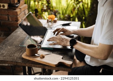 Digital nomad in Bali. A man on a business trip or vacation takes a coffee break in a busy cafe, working on his laptop as he sips. Young man holding mobile phone and coffee cup. 