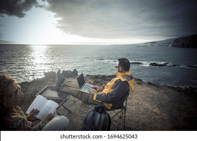 Digital Nomad And Freedom From Office Work Lifestyle - Couple Of Traveler Enjoying The Outdoor Working Activity On The Cliff Looking At The Ocean And Blue Sky - Internet Connection And Travel Life