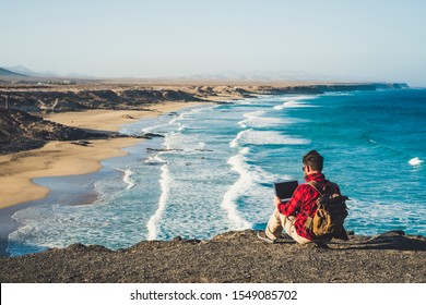 Digital Nomad Lifestyle Concept With Adult Man Sit Down On The Ground With Scenic View Of Beach And Ocean Inbackground - Work With Technology Internet Laptop Computer In Alternative Free Office