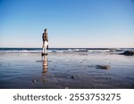 Digital nomad man on the shore of a beach at low tide with a laptop case, looking at the horizon, in Cheng Hai Lou, near Beijing, China