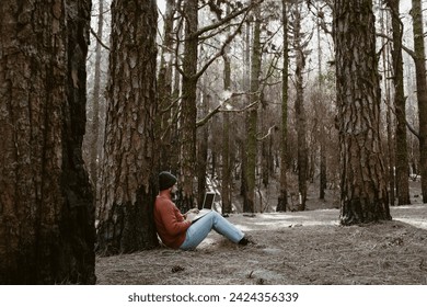 Digital nomad and remote working concept lifestyle people with man sitting ou the ground inside a forest woods using laptop computer and roaming internet modern connection technology. Outdoors leisure