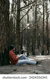 Digital nomad and remote working concept lifestyle people with man sitting ou the ground inside a forest woods using laptop computer and roaming internet modern connection technology. Outdoors leisure