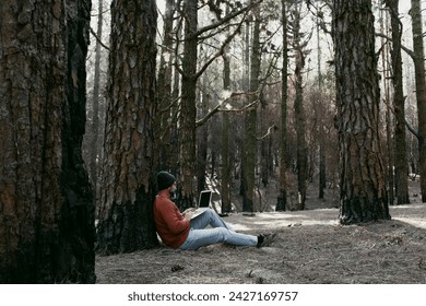 Digital nomad and remote working concept lifestyle people with man sitting ou the ground inside a forest woods using laptop computer and roaming internet modern connection technology. Outdoors leisure