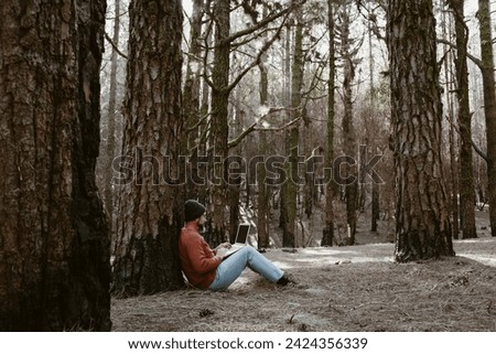 Digital nomad and remote working concept lifestyle people with man sitting ou the ground inside a forest woods using laptop computer and roaming internet modern connection technology. Outdoors leisure