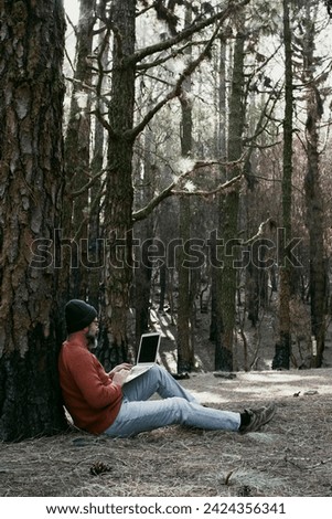 Digital nomad and remote working concept lifestyle people with man sitting ou the ground inside a forest woods using laptop computer and roaming internet modern connection technology. Outdoors leisure