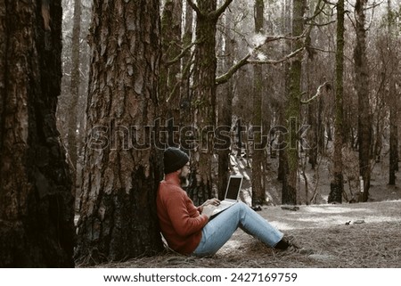 Digital nomad and remote working concept lifestyle people with man sitting ou the ground inside a forest woods using laptop computer and roaming internet modern connection technology. Outdoors leisure