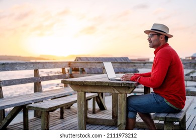 digital nomad sitting outdoors on the table on the beach with a laptop alone doing telecommuting at sunset