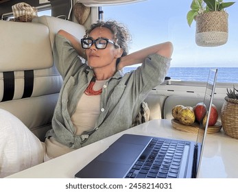 Digital nomad traveler having relax indoor leisure inside a modern motorhome camper van with ocean in background outside the window. Laptop on the table. Remote worker freedom concept lifestyle female - Powered by Shutterstock