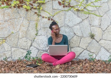 Digital Nomad Woman Working Witth Computer In The Nature. Black Young  Freelancer Sitting On A Call Work Outside. Autumn Leaves.