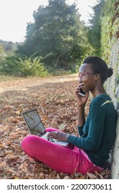 Digital Nomad Woman Working Witth Computer In The Nature. Black Young  Freelancer Sitting On A Call Work Outside. Autumn Leaves.