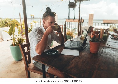 A digital nomad, working with a laptop and talking on the phone, sitting at a wooden table in a cafe.