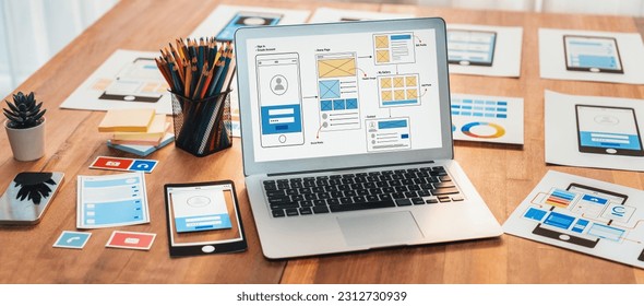 Digital and paper wireframe designs for web or mobile app UI UX display on laptop computer screen. Panoramic shot of developer workspace for brainstorming and design application framework. Scrutinize - Shutterstock ID 2312730939