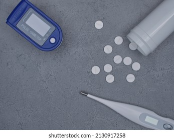 Digital Pulse Oximeter , Thermometer And White Pills On Gray Background. Overhead View With Copy Space.