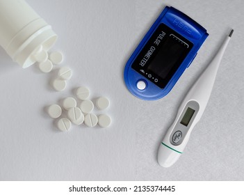 Digital Pulse Oximeter , Thermometer And White Pills On White Background. Overhead View With Copy Space