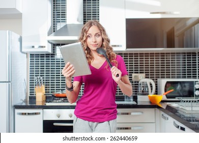 digital recipes book. Thoughtful young woman using digital tablet standing in her kitchen at home