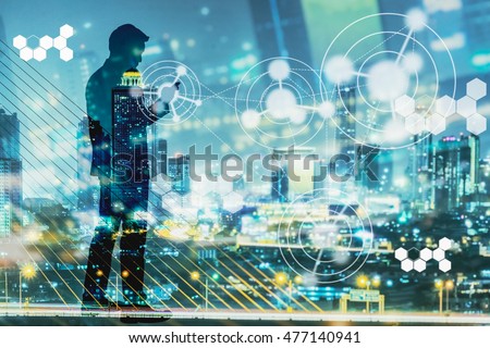 Digital revolution and Internet of Things concept. Double exposure of night city light and silhouette of business man standing and using smart phone with futuristic connection icons.