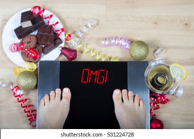 Digital scales with woman feet on them and sign"OMG!" surrounded by christmas decorations, sweets and alcohol. Shows consequences of surfeit and eating unhealthy food during Christmas  holidays. 