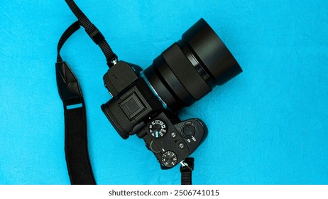 Digital Single-Lens Reflex camera, DSLR camera, black-colored, with lens attached on it, placed on a light blue colored cloth background. DSLR camera with lens