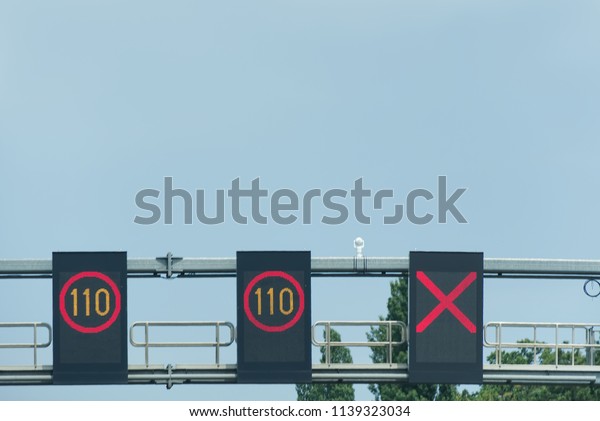 Digital speed\
signs above highway. A red forbidden to drive cross and two plates\
one hundred and ten with blue\
sky