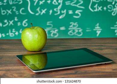 Digital tablet and apple on the desk in front of blackboard