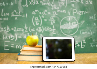 Digital tablet and apple on the desk in front of blackboard