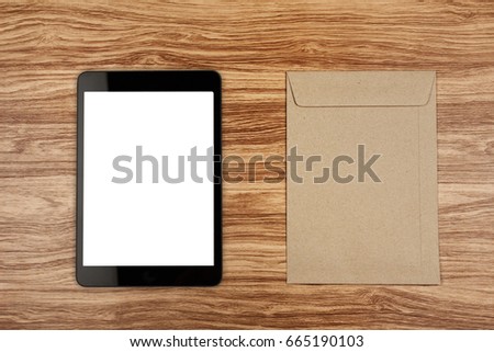 Digital tablet with blank screen and brown envelope on wooden desk