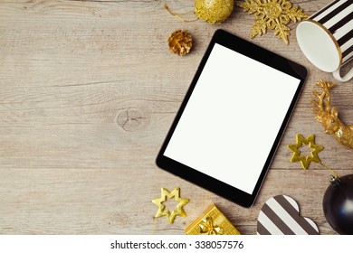 Digital tablet and Christmas golden decorations on wooden background. View from above