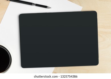 Digital tablet computer and cup of coffee on wooden desk.