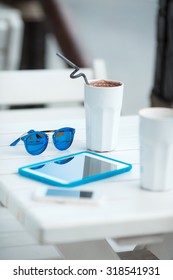 Digital tablet computer with cup of coffee on old wooden table in white cafe. Simple workspace or coffee break with web surfing. bue sunglasses