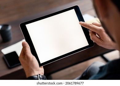 Digital tablet computer device white blank empty screen in male hand over desk tablet mockup image. Business man using modern technology for wireless communication and online work - Powered by Shutterstock