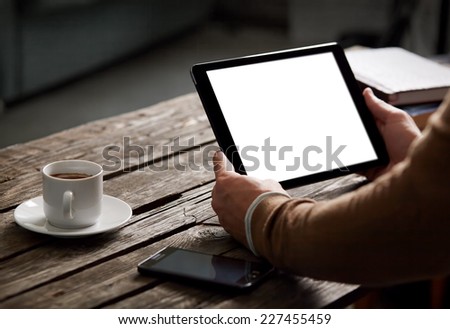 Digital tablet computer with isolated screen in male hands over cafe background - table, smart phone, cup of coffee...