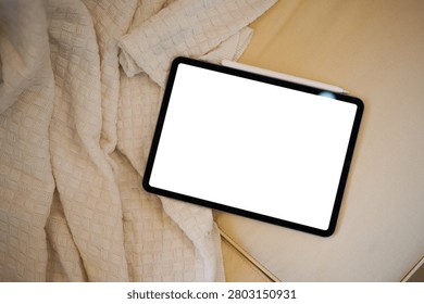 Digital tablet displaying empty white screen with stylus pen resting on a beige sofa, perfect for app UI mockup and technology lifestyle concepts.