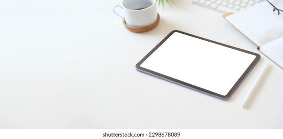 Digital tablet with empty screen on coffee cup and notepad on white office desk. Copy space for your text.