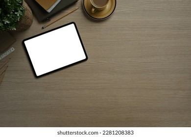 Digital tablet, notepad, coffee cup and potted plant on wooden table. White screen for for your advertising text message