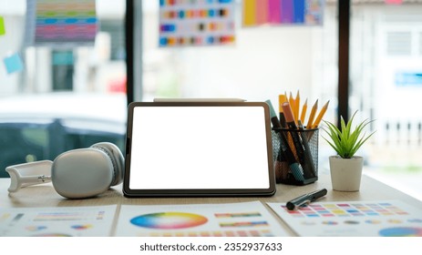 Digital tablet with white empty screen, headphone, color swatch samples and stationery on graphic designer workspace.