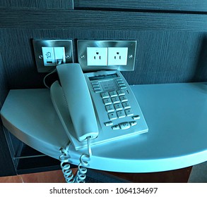 Digital Telephone On A White Table, With Power Outlets And USB Outlet On The Wall 